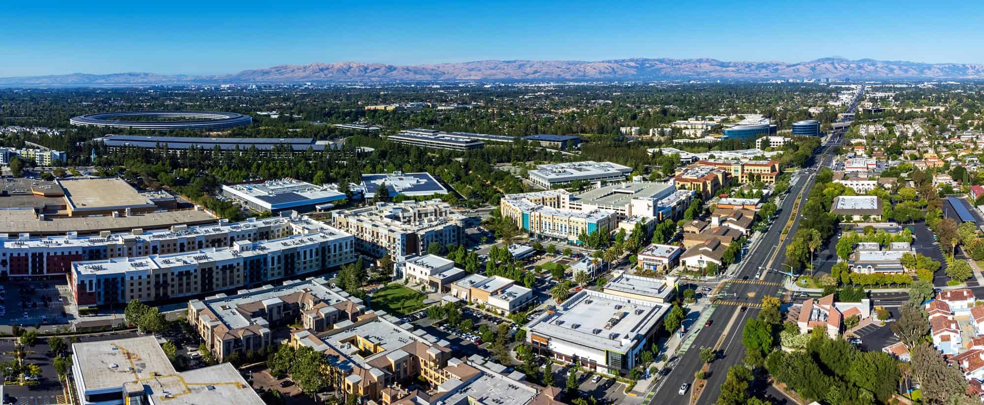 Vista aérea do Vale do Silício, na Califórnia, com edifícios comerciais, áreas residenciais, vegetação e o Apple Park ao fundo